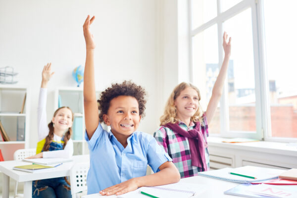 Elementary students raising hands during a reading comprehension lesson